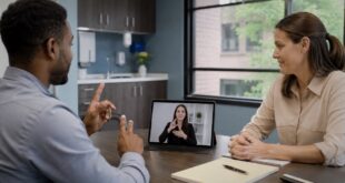Deaf man using sign language during a meeting while a remote interpreter appears on a tablet screen.