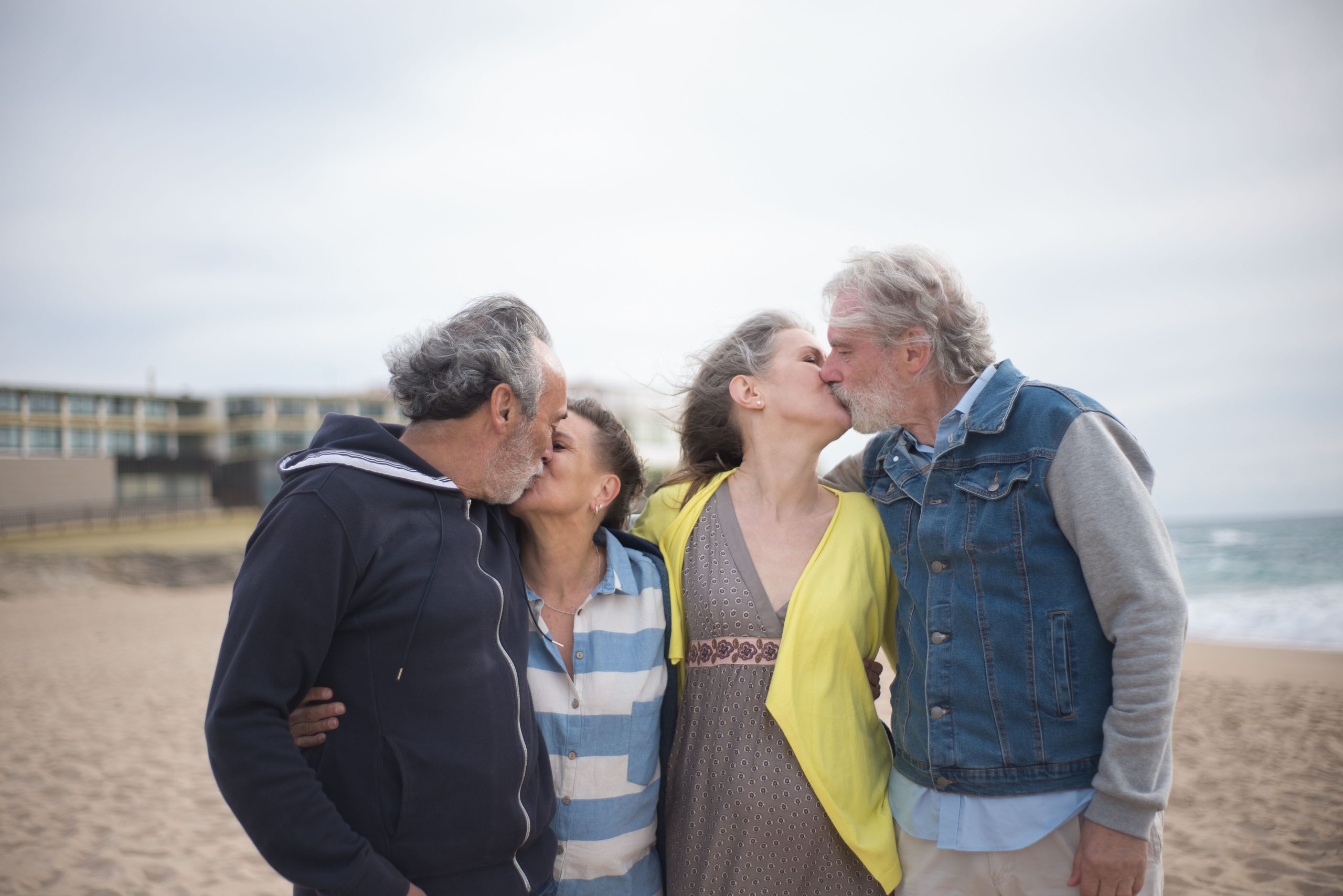 Younger and older couples sharing affectionate moments on a beach, illustrating changing ideas about romance across generations.