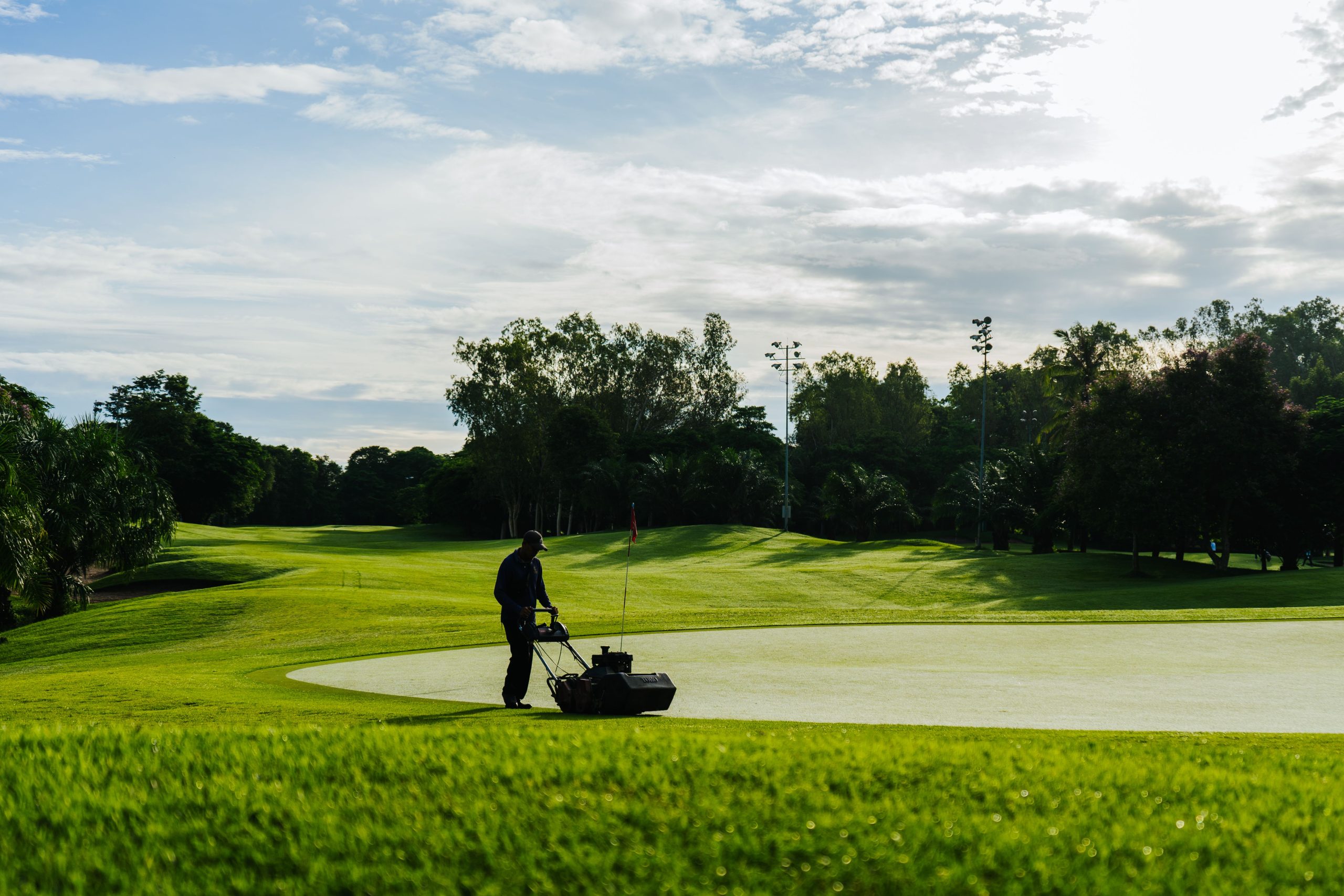 Groundskeeper mowing even stripes across a lush golf-course lawn