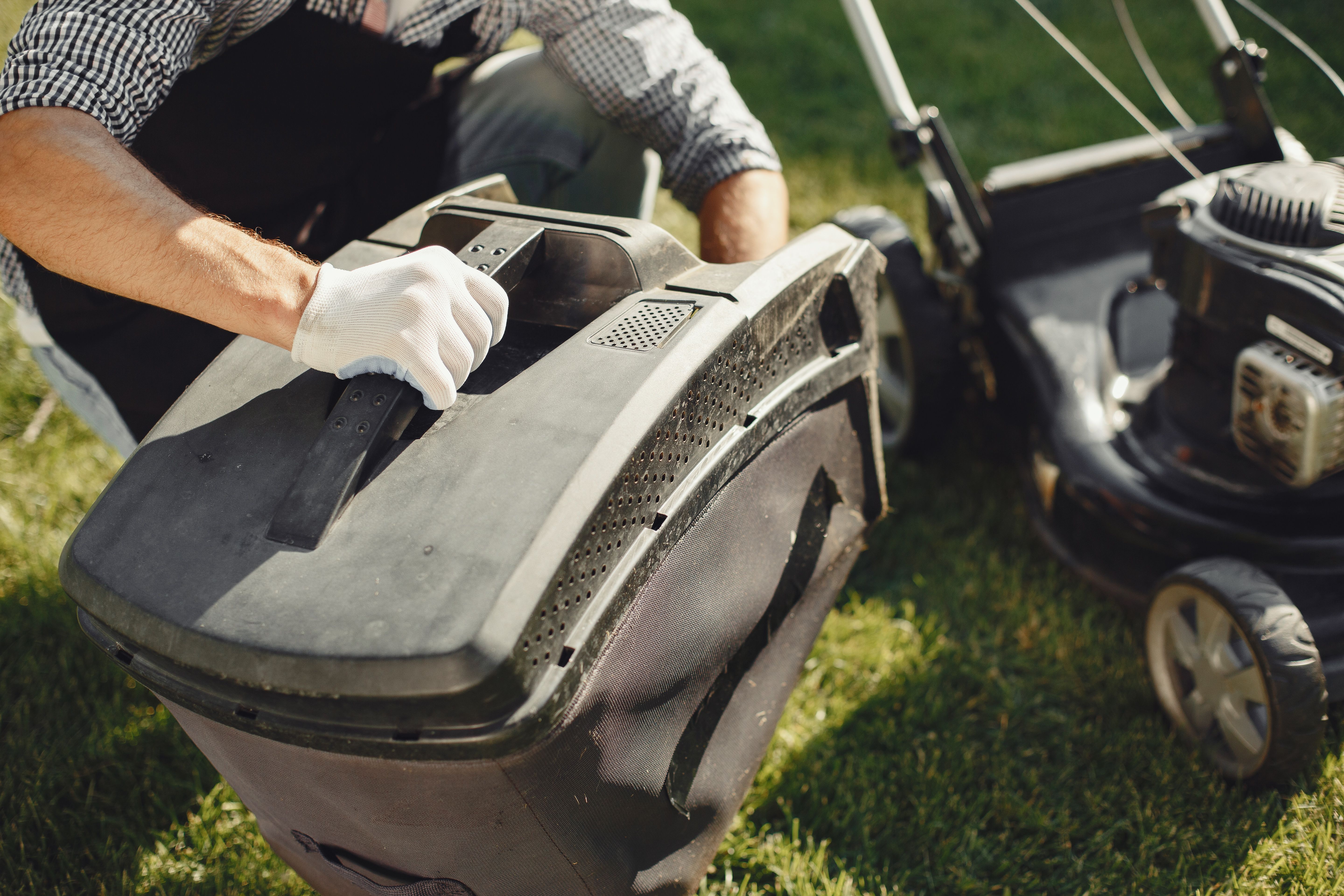 Homeowner fitting a grass catcher bag to a lawnmower before mowing