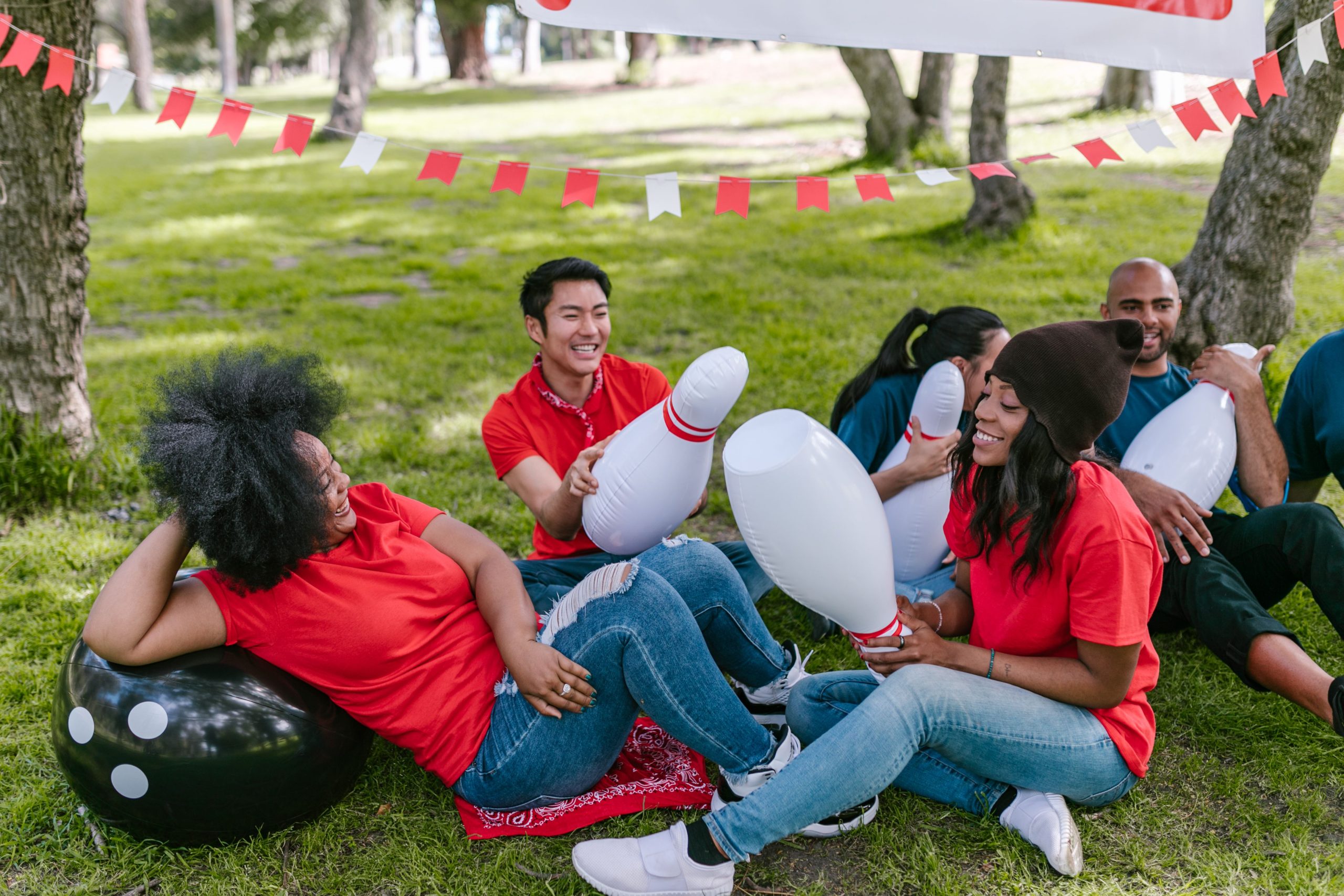 A diverse group laughing and taking part in an outdoor team-building game in a park.
