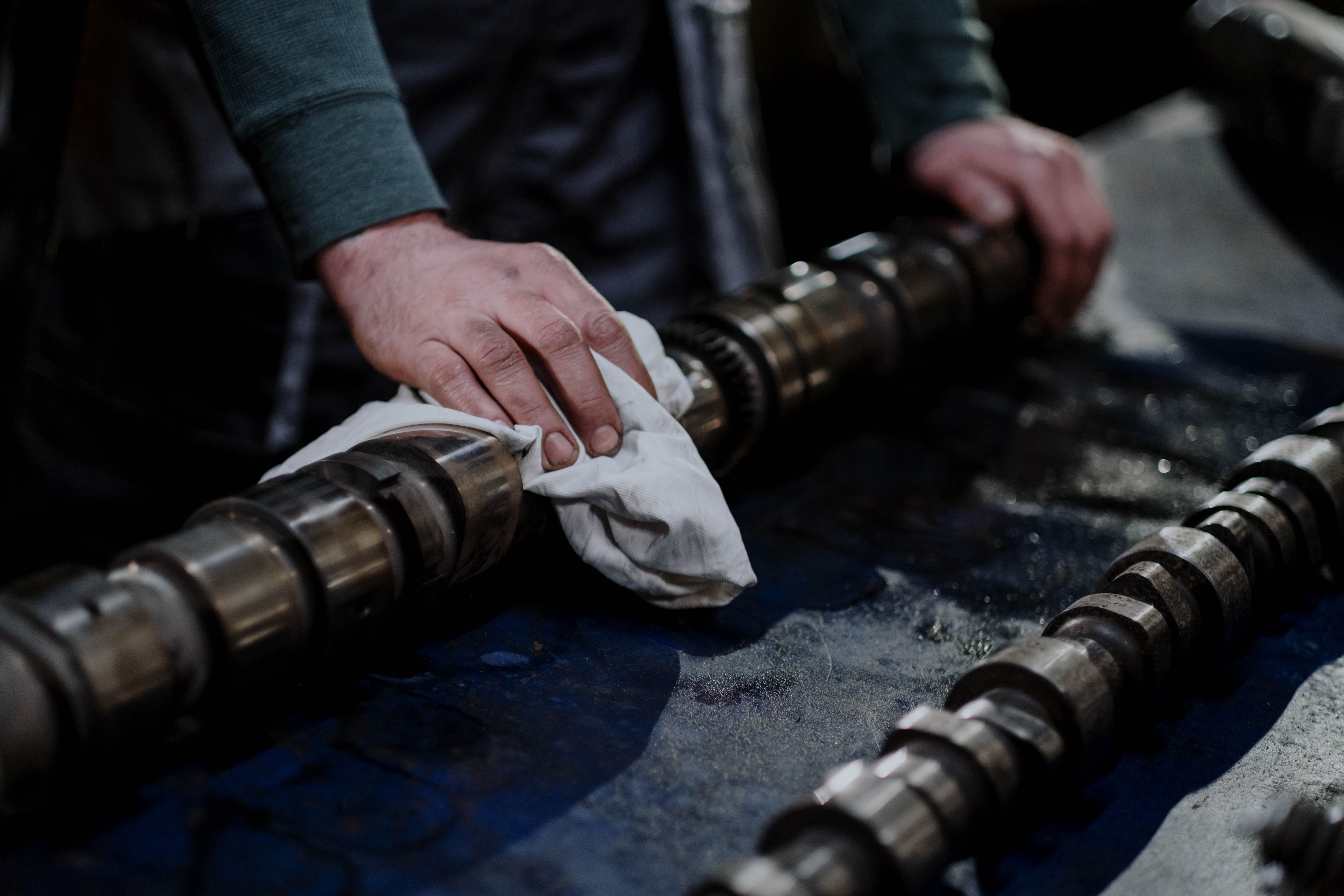 Mechanic cleaning a camshaft, illustrating inspection and refurbishment of tractor engine parts.